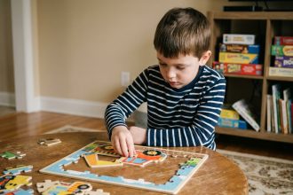 Enfant concentré assemblant un puzzle de construction en bois sur une table ronde dans un salon chaleureux